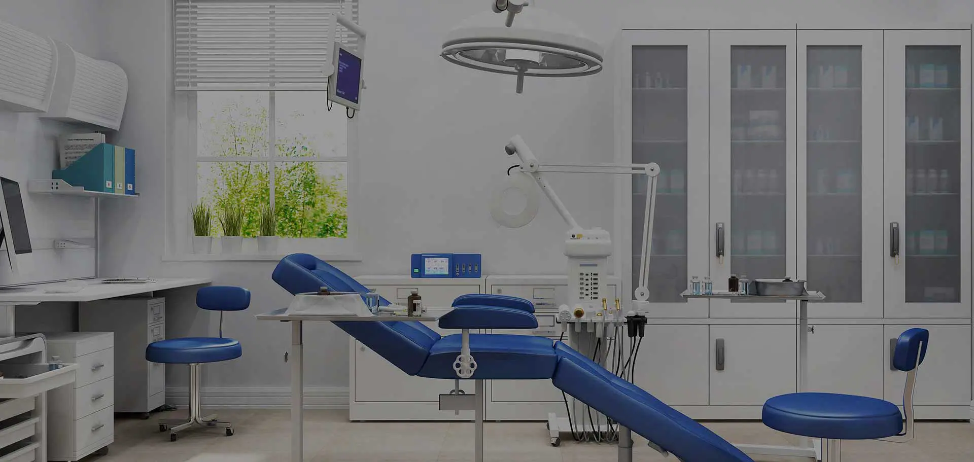 Modern medical office with a blue examination chair, overhead light, and medical equipment. Cabinets and a window with greenery create a clean, calm atmosphere.
